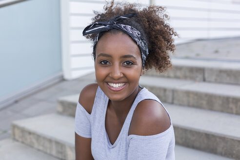 Portrait of smiling young woman wearing hair-band sitting on stairs - JUNF01492