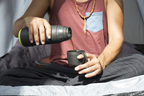 Mann sitzt im Zelt und gießt Kaffee in eine Tasse, Teilansicht, lizenzfreies Stockfoto