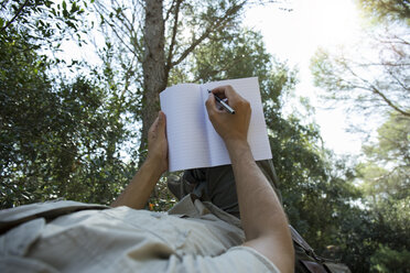 Man lying in hammock writing in notebook, partial view - JPTF00009