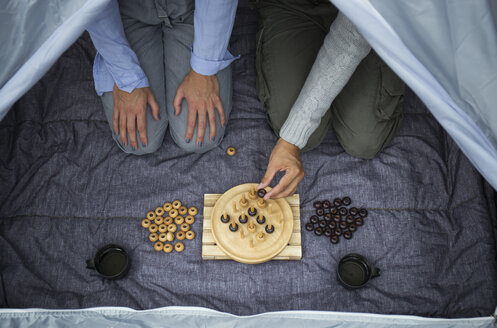 Couple sitting in tent playing board game, partial view - JPTF00014