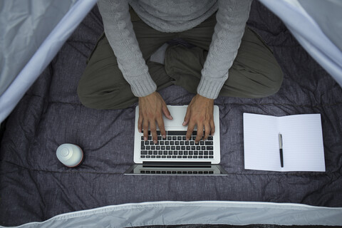 Mann sitzt im Zelt und arbeitet am Laptop, Teilansicht, lizenzfreies Stockfoto