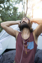 Porträt eines Mannes vor einem Zelt, der mit Kopfhörern Musik hört - JPTF00020