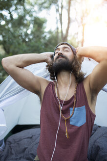 Portrait of man in front of tent listening music with earphones - JPTF00020