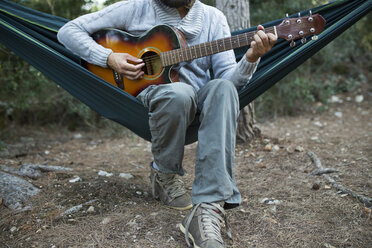 Mann sitzt in Hängematte und spielt Gitarre im Wald, Teilansicht - JPTF00021