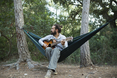 Mann sitzt in Hängematte und spielt Gitarre im Wald, Teilansicht - JPTF00022