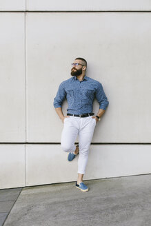 Bärtiger Hipster-Geschäftsmann mit Brille und kariertem Hemd lehnt an der Wand - FMGF00011