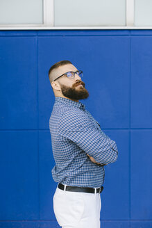 Porträt eines bärtigen Hipster-Geschäftsmannes mit kariertem Hemd vor einem blauen Hintergrund - FMGF00015