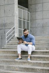 Bärtiger Hipster-Geschäftsmann sitzt auf einer Treppe und benutzt ein digitales Tablet - FMGF00023