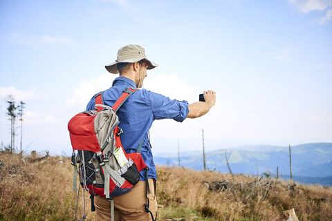 Mann fotografiert beim Wandern mit seinem Handy, lizenzfreies Stockfoto