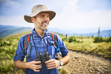 Lächelnder Mann mit Fernglas beim Wandern in den Bergen - BSZF00671