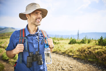 Lächelnder Mann mit Fernglas beim Wandern in den Bergen - BSZF00674