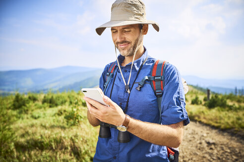 Lächelnder Mann, der beim Wandern sein Handy überprüft - BSZF00675