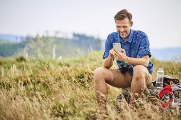 Lächelnder Mann, der sich beim Wandern ausruht und sein Mobiltelefon überprüft - BSZF00681