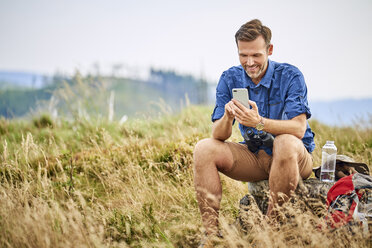 Smiling man resting and checking his cell phone during hiking trip - BSZF00681