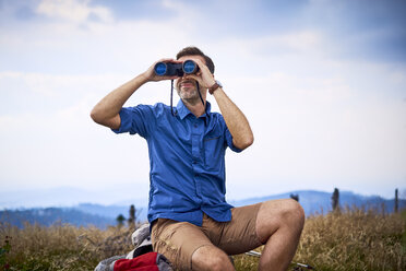 Mann schaut beim Wandern durch ein Fernglas - BSZF00684