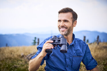 Lächelnder Mann mit Fernglas beim Wandern in den Bergen - BSZF00685