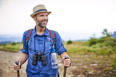 Lächelnder Mann mit Fernglas beim Wandern in den Bergen - BSZF00694