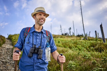 Lächelnder Mann mit Fernglas beim Wandern in den Bergen - BSZF00697