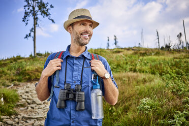 Lächelnder Mann mit Fernglas beim Wandern in den Bergen - BSZF00699