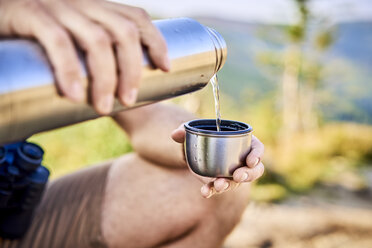 Close-up of man during hiking trip pouring cold water from thermos flask - BSZF00715