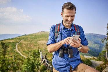 Lächelnder Mann, der beim Wandern sein Handy überprüft - BSZF00718