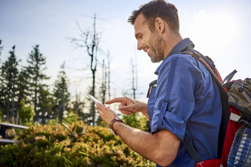 Lächelnder Mann, der beim Wandern sein Handy überprüft - BSZF00719