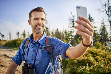 Man taking a selfie with his cell phone during hiking trip in the mountains - BSZF00720