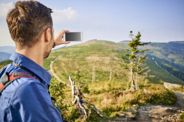 Man taking picture with his cell phone during hiking trip in the mountains - BSZF00721