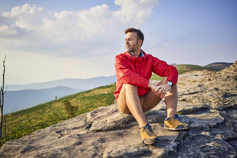 Mann sitzt auf einem Felsen und genießt ruhige Momente beim Wandern, lizenzfreies Stockfoto