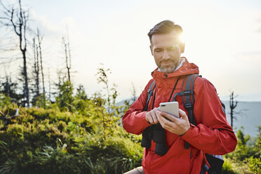 Smiling man checking his cell phone during hiking trip - BSZF00740