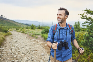 Lächelnder Mann mit Fernglas beim Wandern in den Bergen - BSZF00744