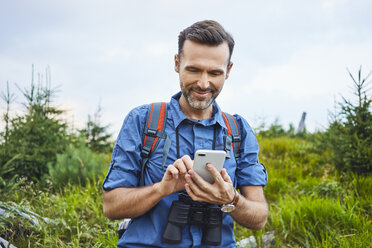 Lächelnder Mann, der beim Wandern sein Handy überprüft - BSZF00747