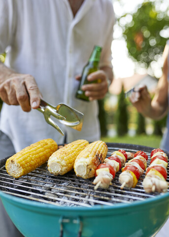 Corn cob and meat skewer on grill at barbecue in garden stock photo