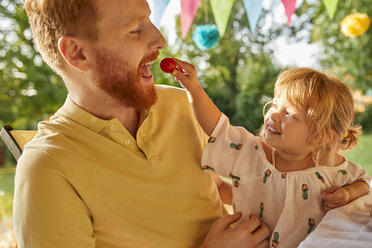 Daughter feeding father with tomato on a garden party - ZEDF01603