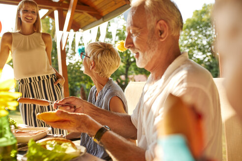 Älterer Mann bei der Zubereitung eines Hotdogs auf einer Gartenparty - ZEDF01623