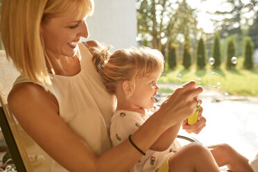 Happy mother and daughter blowing soap bubbles on porch - ZEDF01632