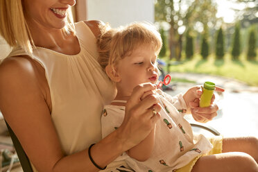 Happy mother and daughter blowing soap bubbles on porch - ZEDF01633