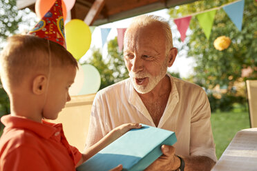 Grandfather handing over present to grandson on a garden birthday party - ZEDF01653