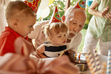 Grandfather and grandchildren blowing out candles on birthday cake on a garden party - ZEDF01672