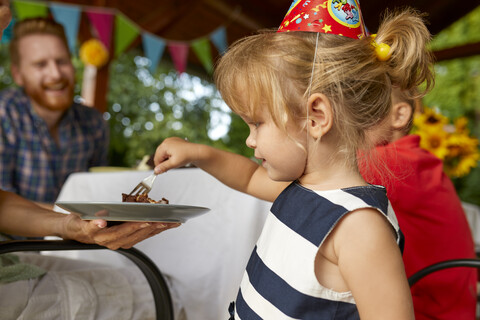 Kleines Mädchen isst Kuchen auf einer Geburtstagsparty im Garten, lizenzfreies Stockfoto