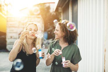 Zwei glückliche Frauen beim Seifenblasenblasen im Freien - HMEF00023