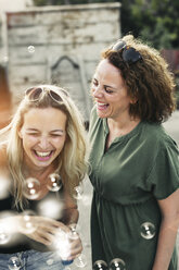 Two happy women with soap bubbles outdoors - HMEF00024