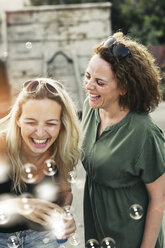 Zwei glückliche Frauen mit Seifenblasen im Freien - HMEF00024