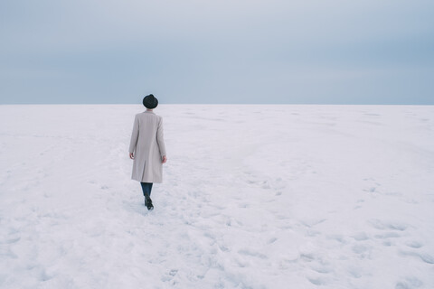 Frau in Mantel und Hut geht in verschneiter Landschaft spazieren, lizenzfreies Stockfoto