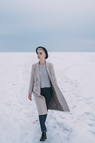 Frau in Mantel und Hut geht in verschneiter Landschaft spazieren, lizenzfreies Stockfoto