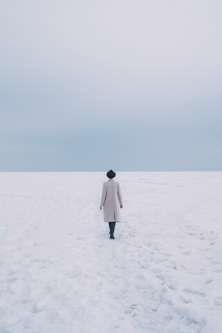 Frau in Mantel und Hut geht in verschneiter Landschaft spazieren, lizenzfreies Stockfoto