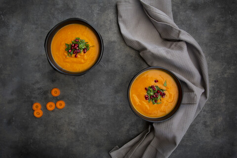 Bowl of carrot ginger coconut soup with topping of parsley and pomegranate seed stock photo