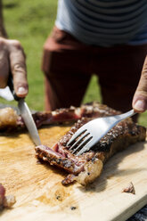 Mann schneidet Fleisch auf einem Holzbrett im Freien, Nahaufnahme - VABF01628