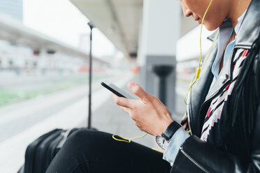 Frau auf dem Bahnsteig sitzend, Smartphone benutzend, Kopfhörer tragend, Mittelteil - CUF45184