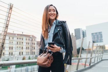 Businesswoman walking outdoors, holding smartphone, smiling - CUF45203